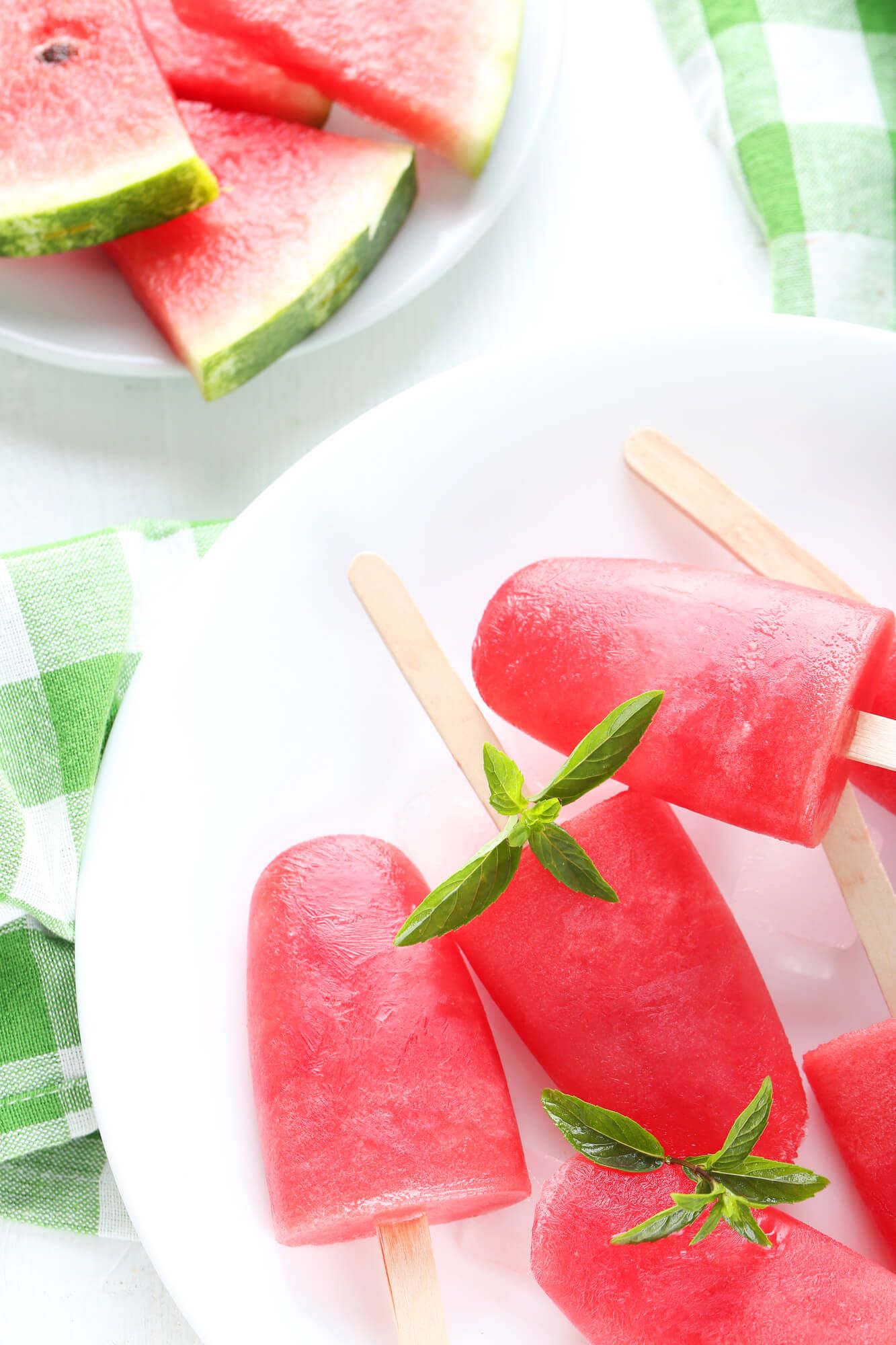 Watermelon popsicles and pieces of fresh watermelon on a white counter.