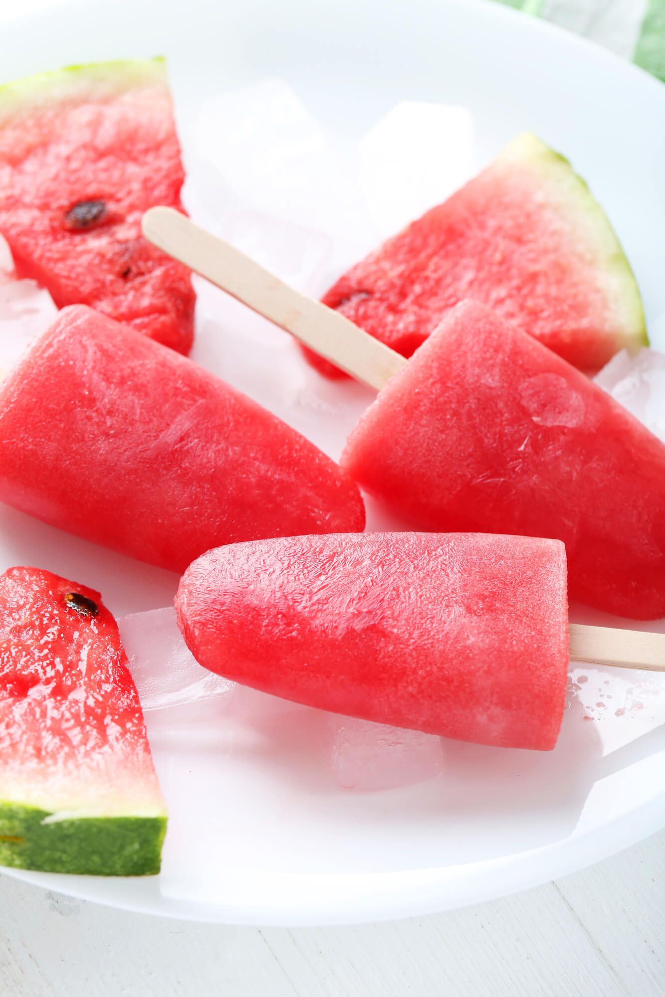 Watermelon Strawberry Popsicles on a dish with fresh watermelon.
