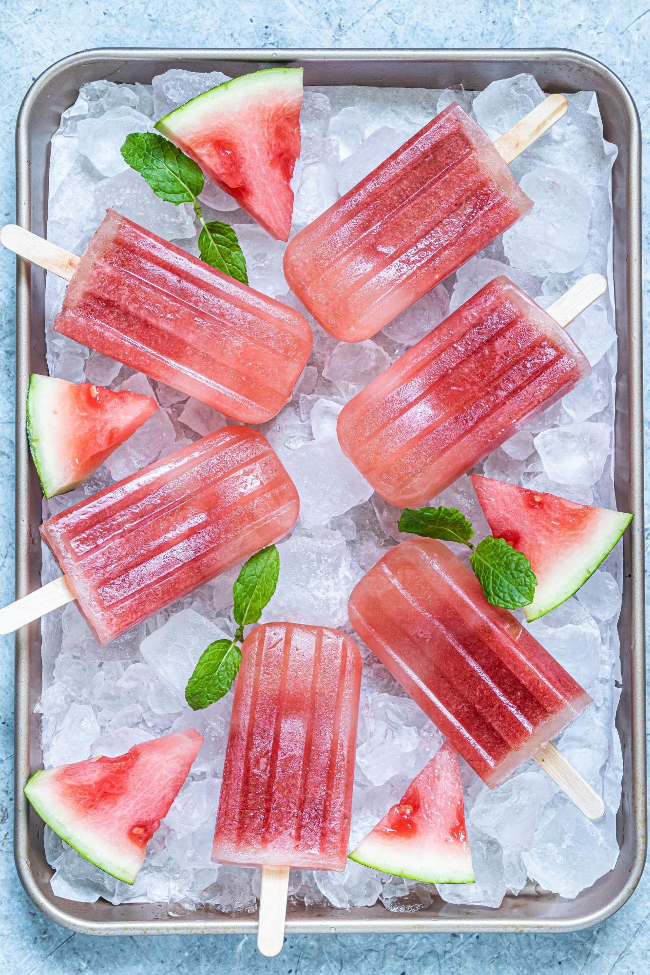 Popsicles with fresh watermelon on a baking sheet with ice cubes, fresh mint, and watermelon.
