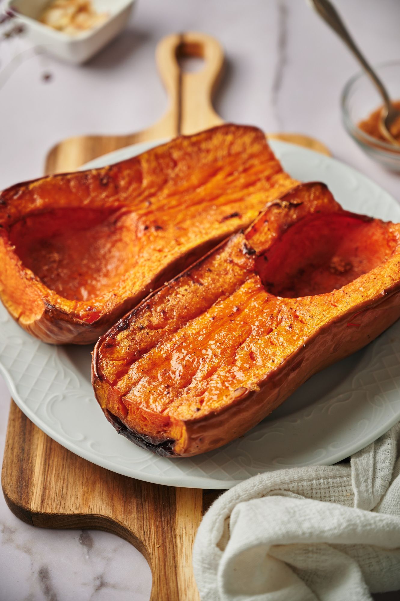 Roasted whole butternut squash drizzled with olive oil, brown sugar, salt, and pepper on a serving plate.