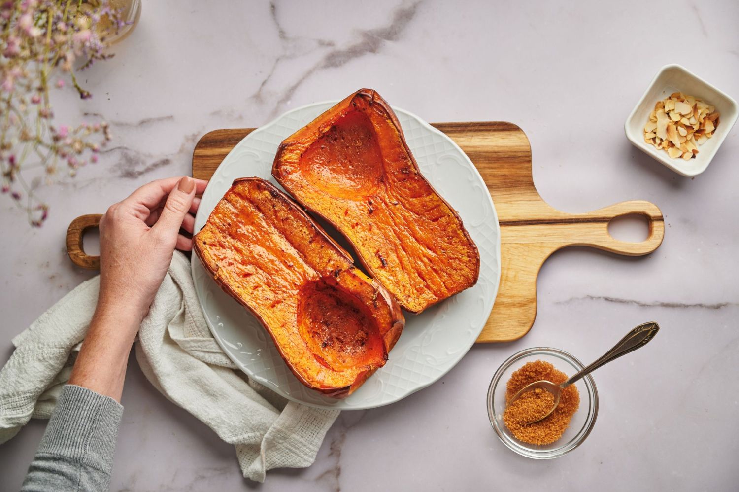 Roasted butternut squash cut in half and roasted whole on a white plate with brown sugar and garlic on the side.