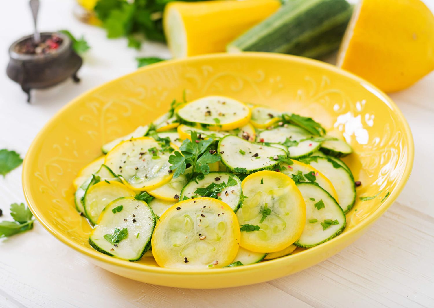 Recipes for yellow squash salad with zucchini and herbs in a bowl with a spoon.