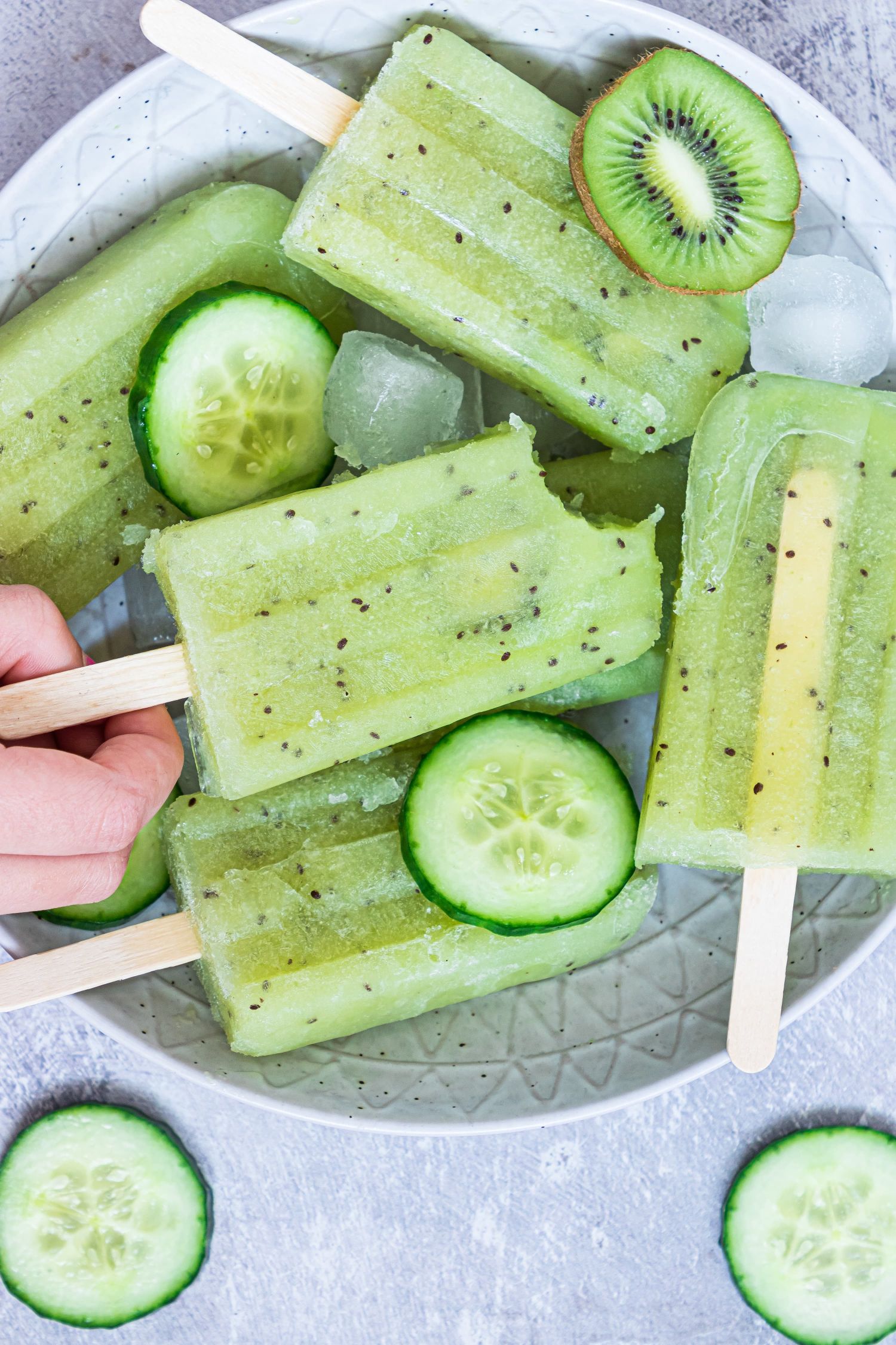 Homemade cucumber popsicles with fresh slices of cucumber and kiwi on a plate.