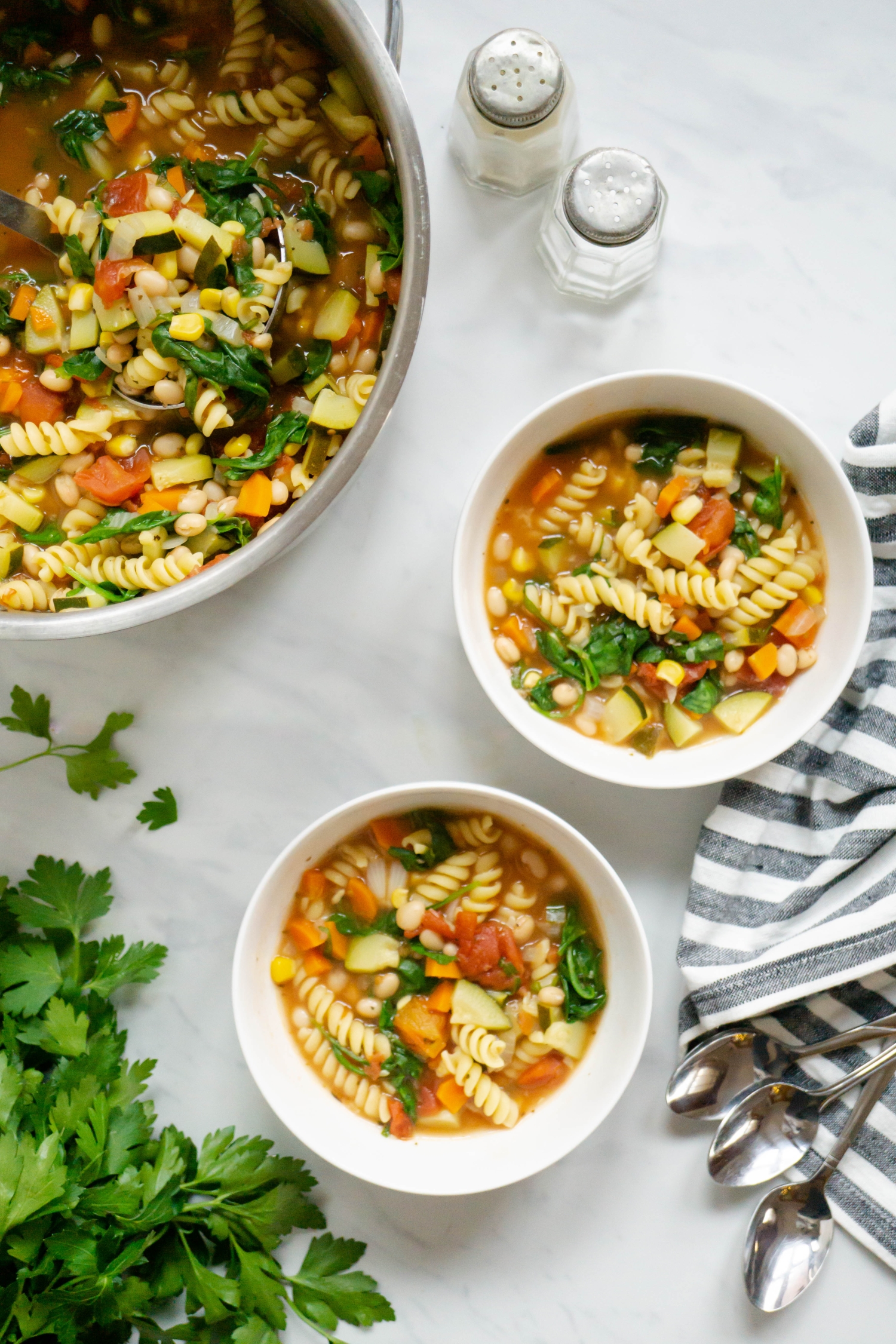 Garden minestrone soup in two bowls with fresh vegetables, pasta, and white beans.