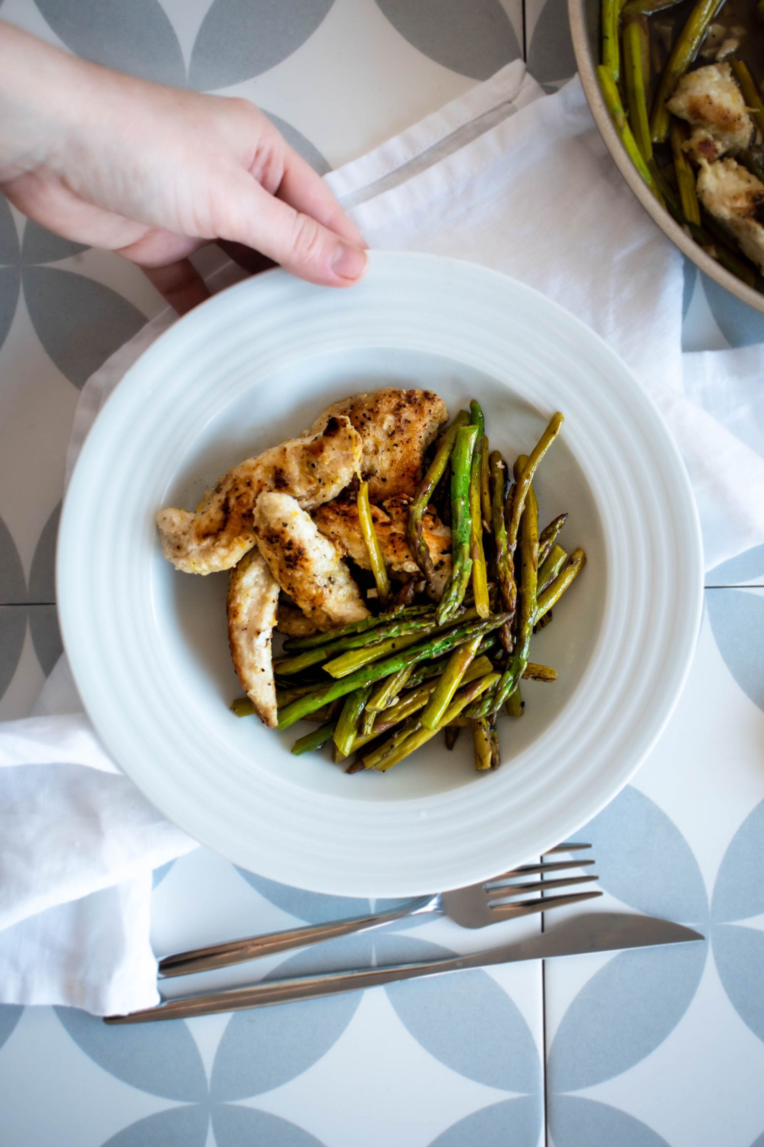 Chicken and asparagus in a lemon garlic sauce served on a plate with a fork and knife on the side.