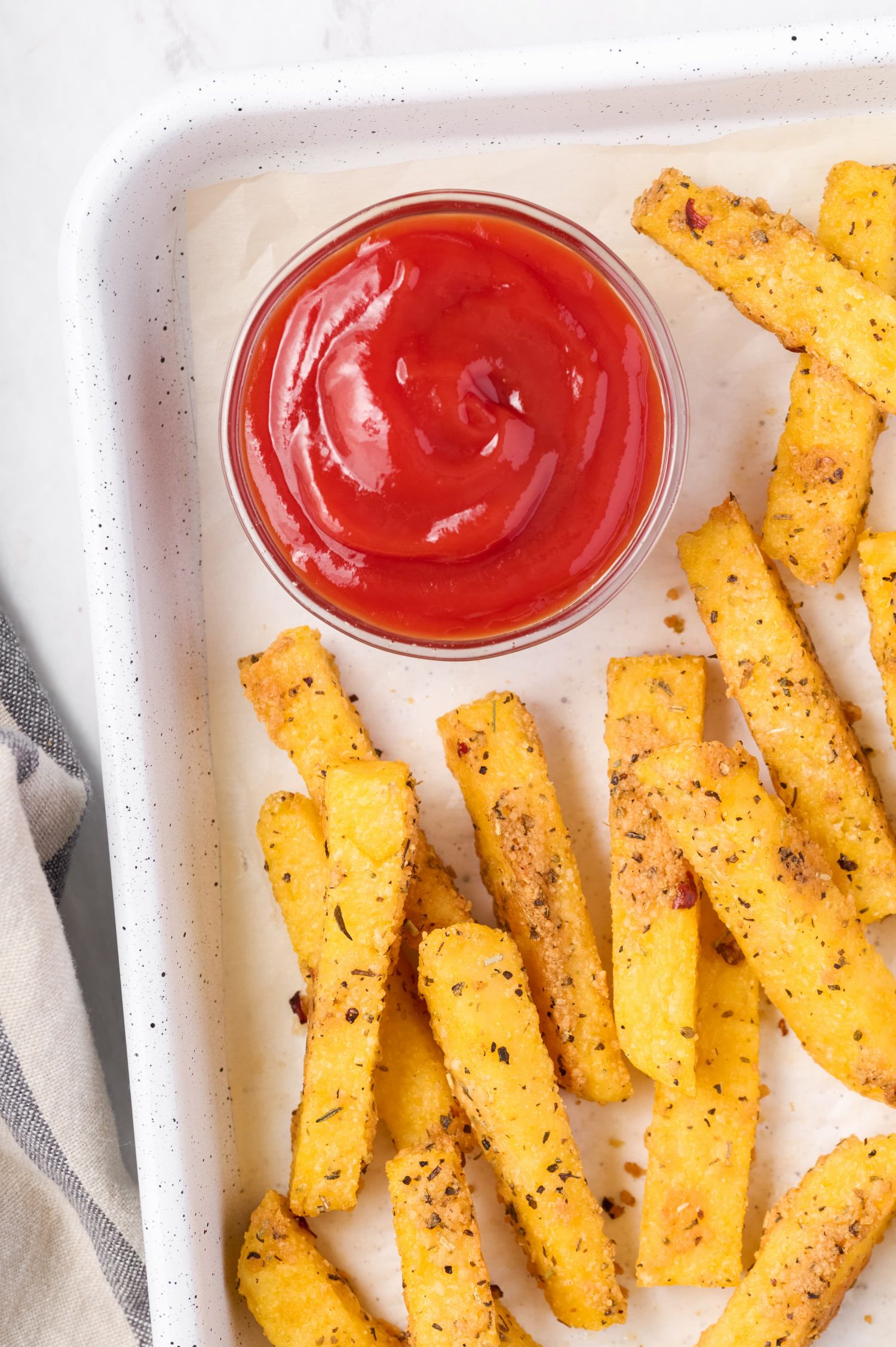 Oven baked polenta fries with crispy browned edges on a baking sheet with ketchup.