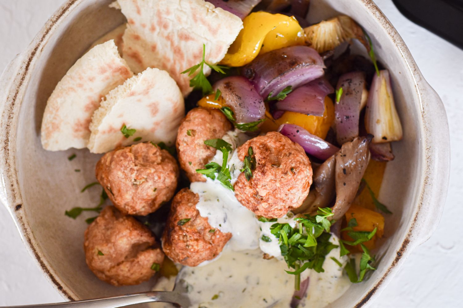 Chicken feta meatballs in a bowl with roasted vegetables pita bread, and tzatziki sauce.