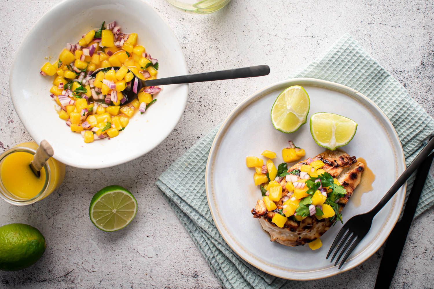 Grilled chicken with mango salsa on a white plate with limes.