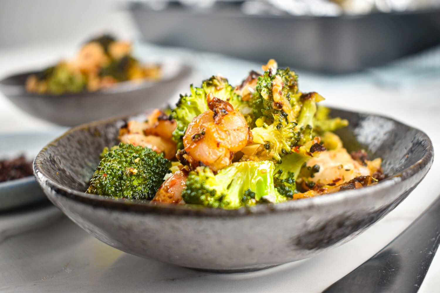 Garlic parmesan shrimp and brocoli in a gray bowl with sprinkled cheese on top.