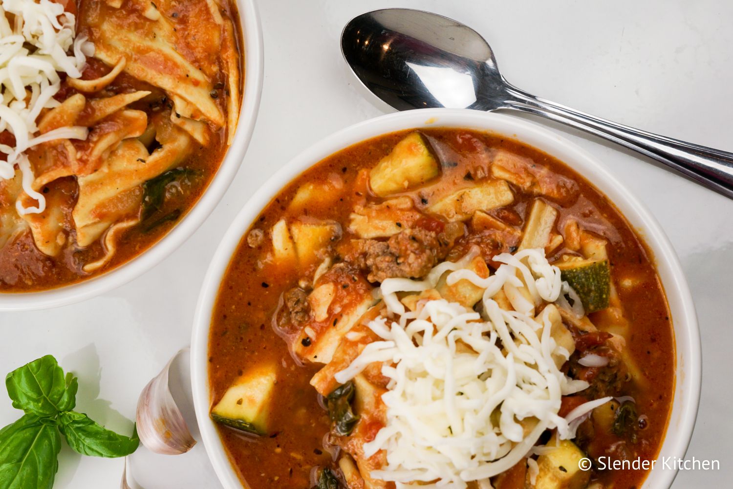 Lasagna soup with vegetables and turkey in two bowls with shredded cheese on top.