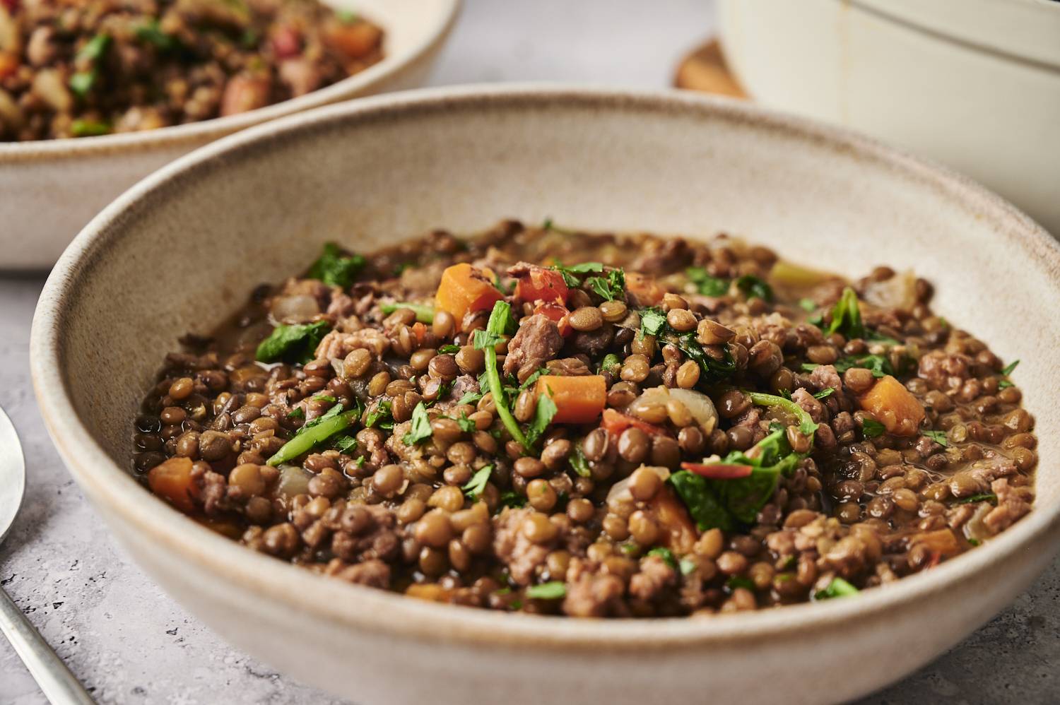 Hearty lentil and sausage soup with diced vegetables, ground meat, and fresh parsley in a shallow ceramic bowl