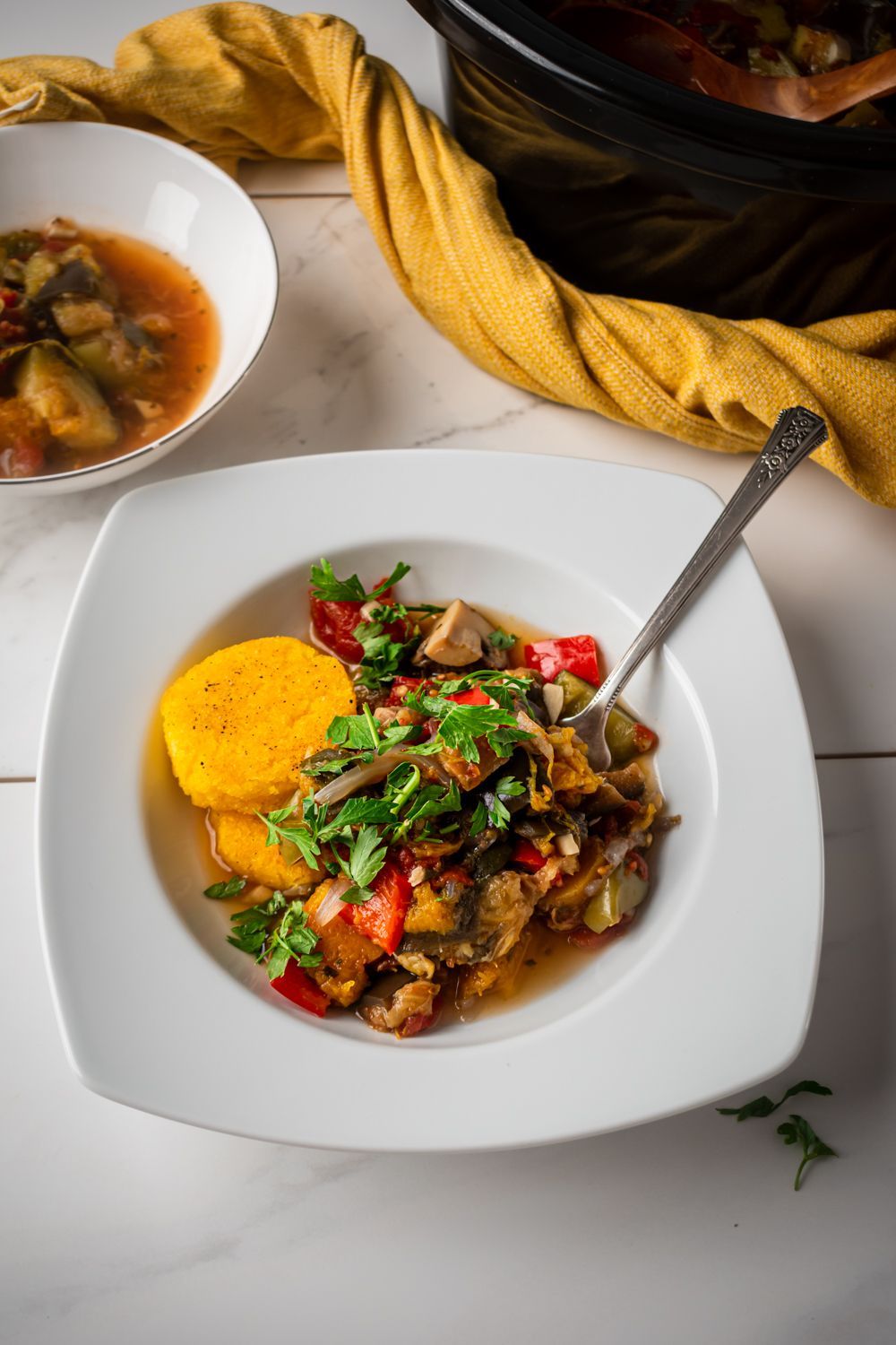 French ratatouille stew in a bowl with eggplant, zucchini, summer squash, and tomatoes topped with fresh herbs and served with crispy polenta