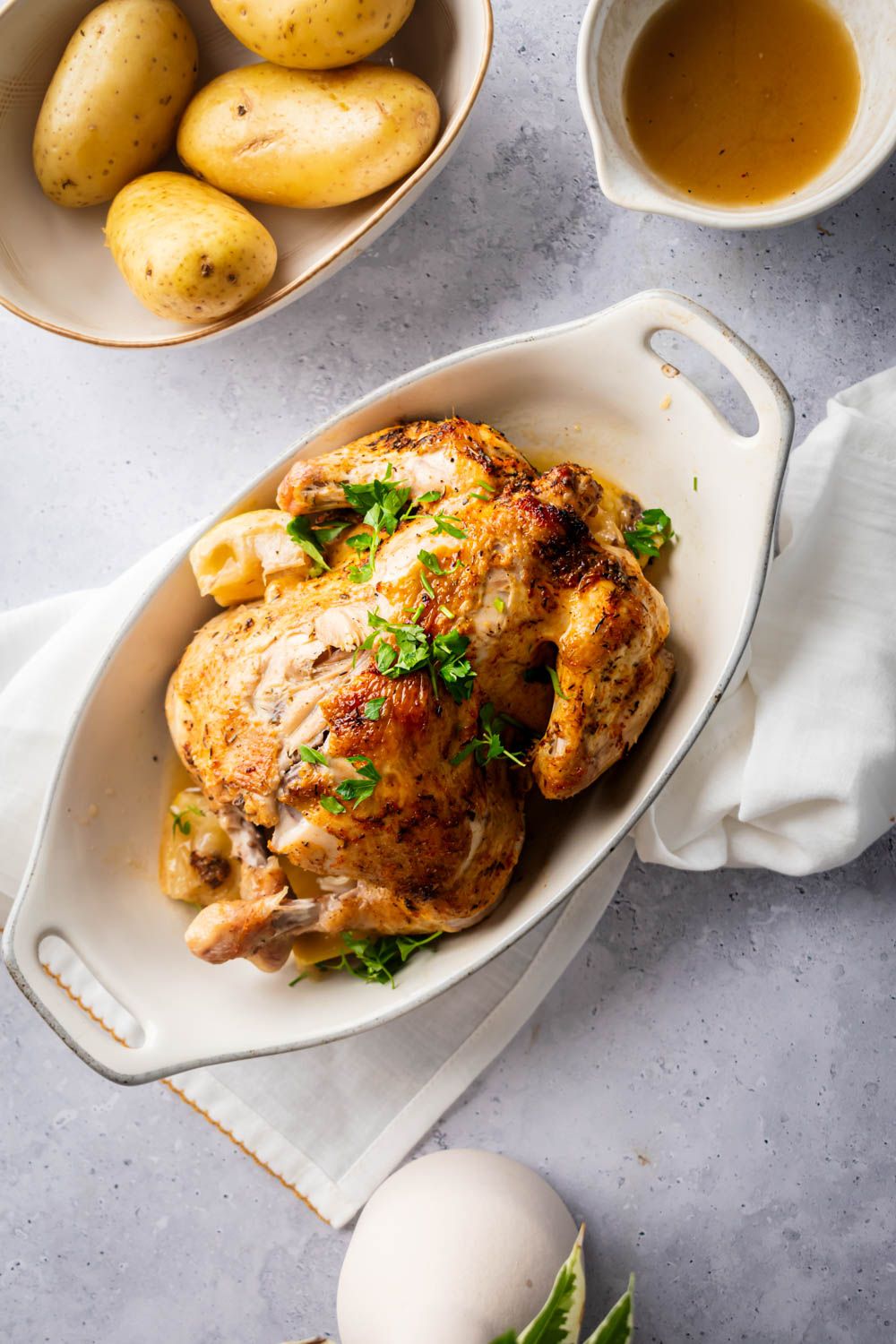 Rotisserie chicken with potatoes served in a white dish with lemon, garlic, and parsley.