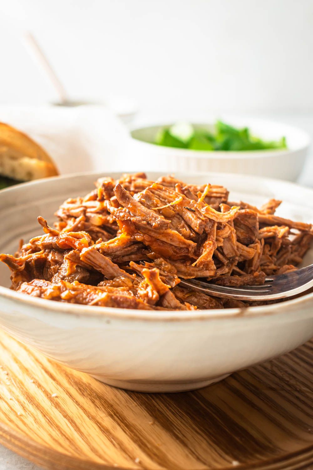Crockpot Italian shredded beef served in a white bowl with a tomato and red wine sauce.