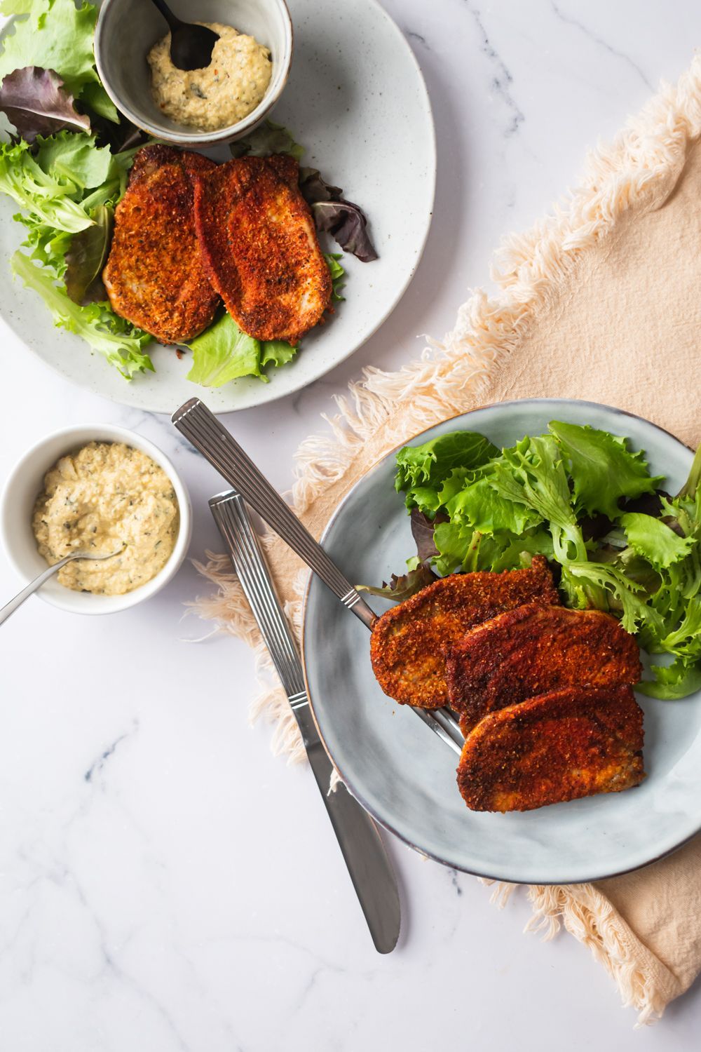 Baked spiced pork chops with a crispy spice rub on a plate with green salad and mustard sauce