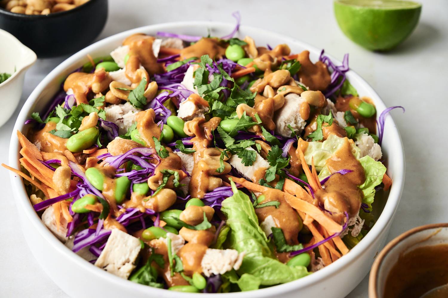 A vibrant salad featuring purple cabbage, edamame, carrots, chicken, and cilantro, drizzled with peanut sauce.