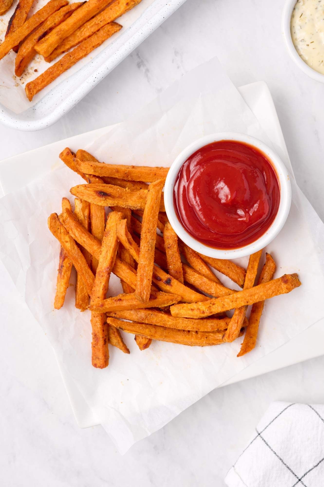 Oven baked sweet potato fries with ketchup served on parchment paper.