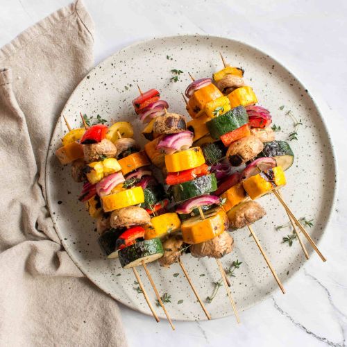 Grilled vegetable skewers seen from above on a beautiful round plate pictured on a marble top table. 