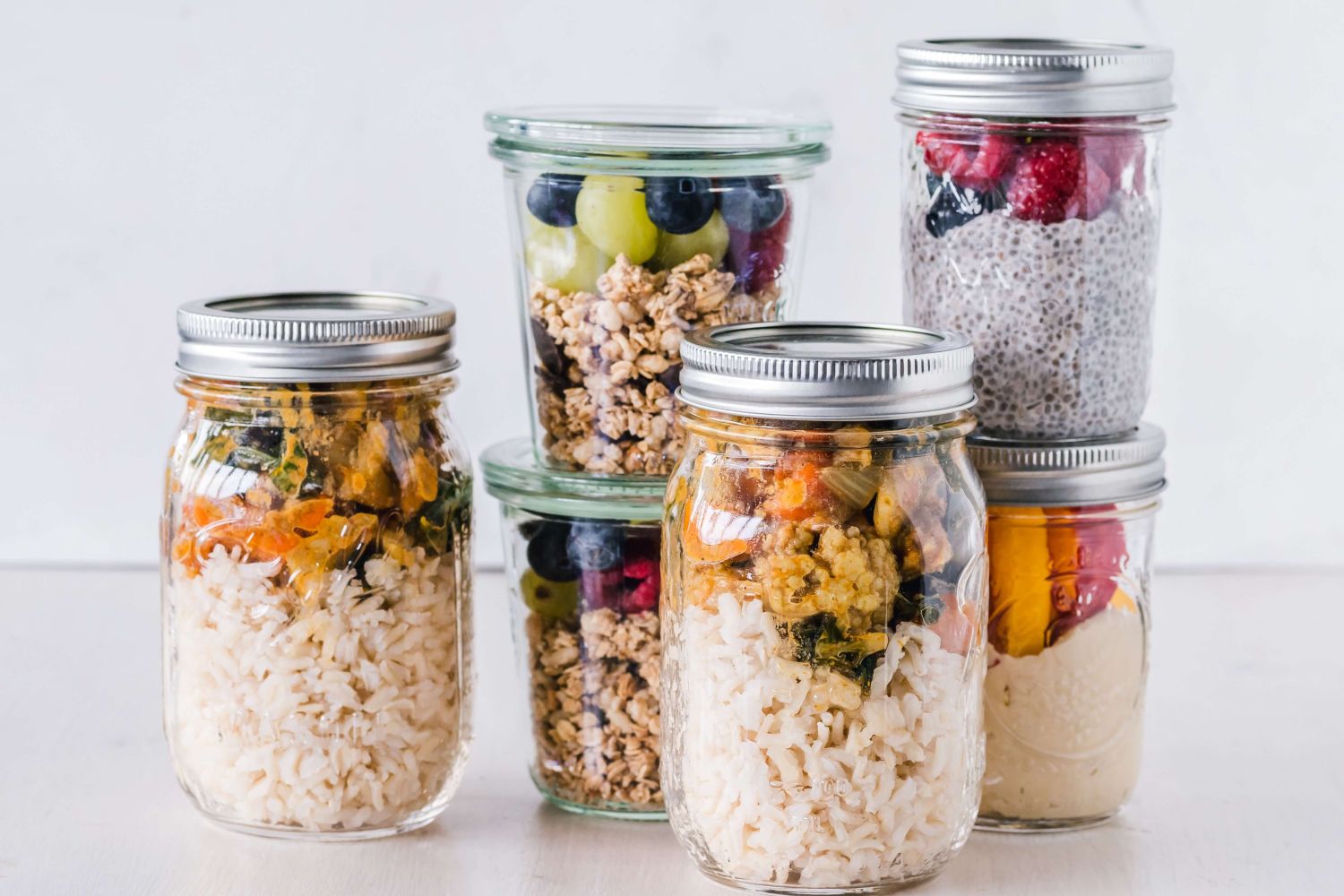 Healthy meal planning jars with salad, granola, hummus, brown rice, and ground chicken.