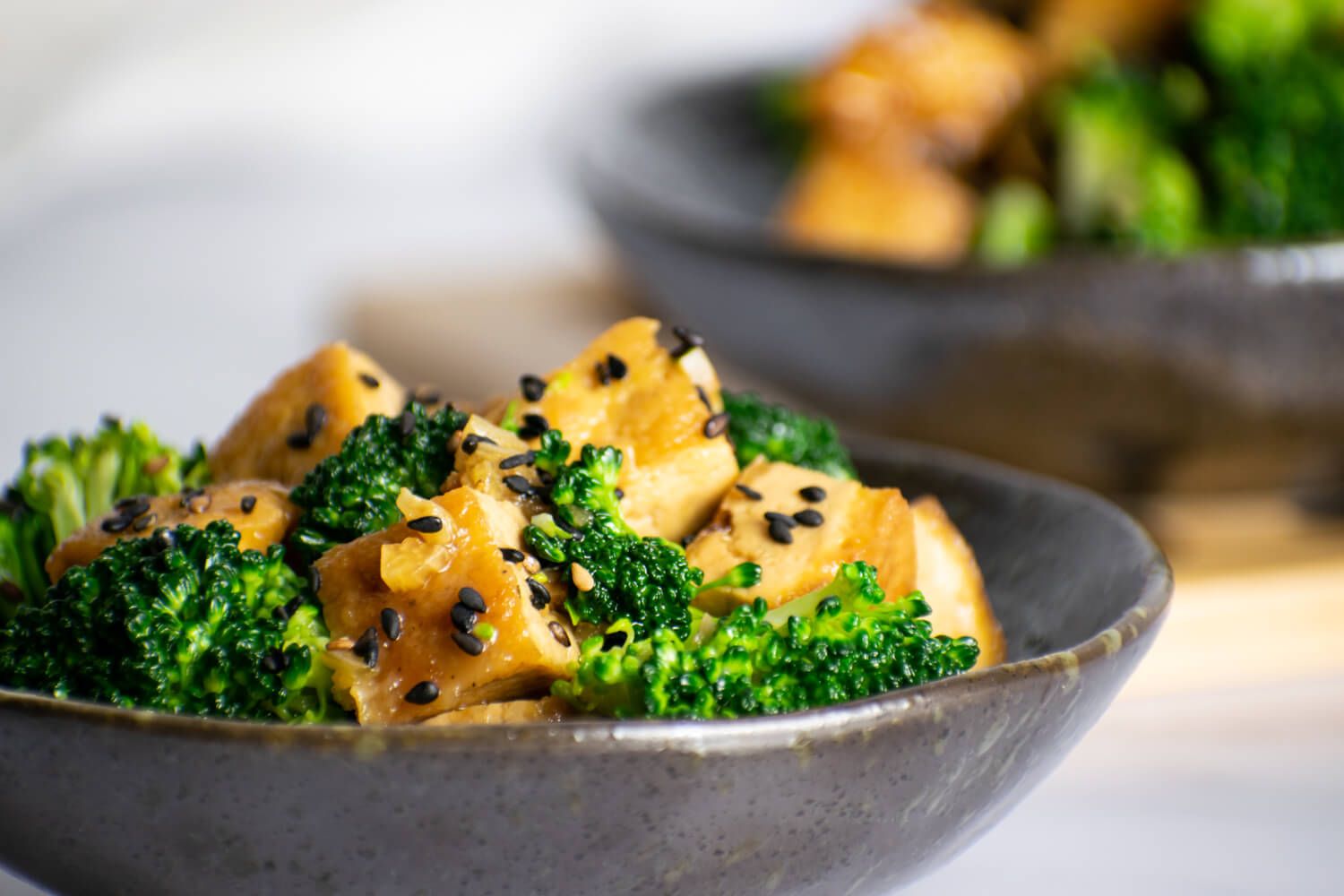 Sesame tofu with broccoli and sesame seeds in a small gray bowl.