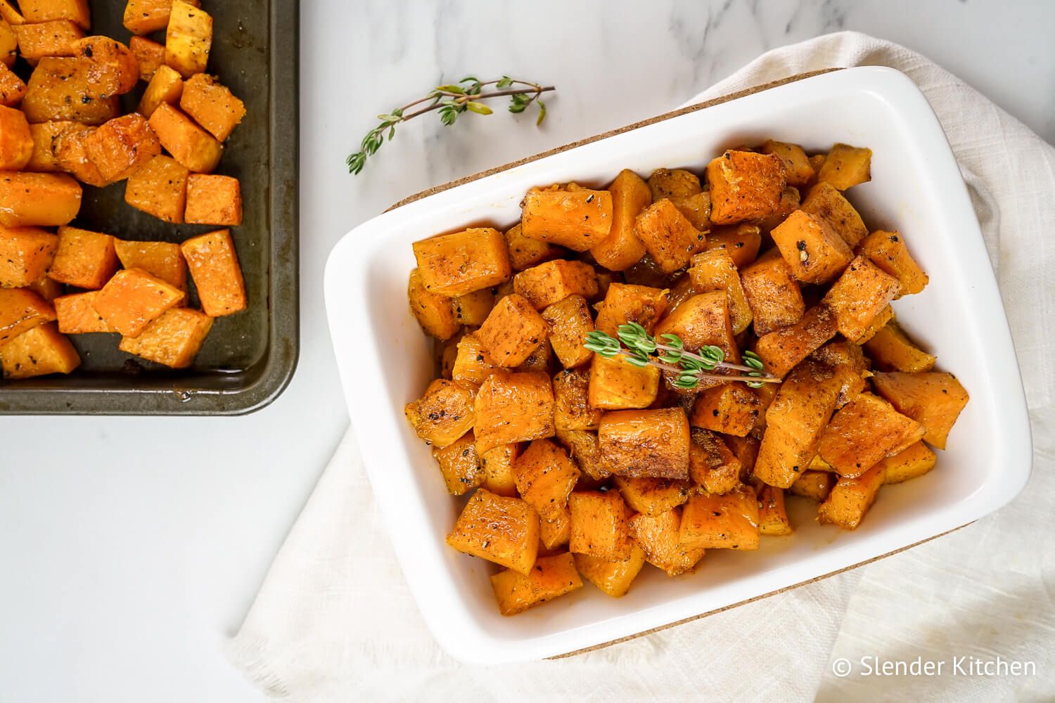 Cinnamon roasted butternut squash in a white dish with a baking sheet. 