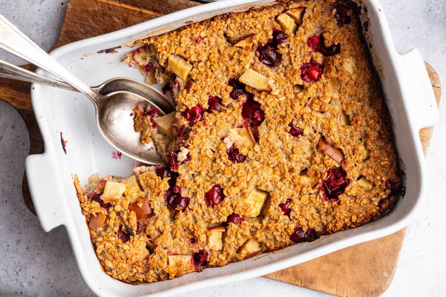 Golden-baked oatmeal casserole with cranberry and apple chunks in a white dish. 