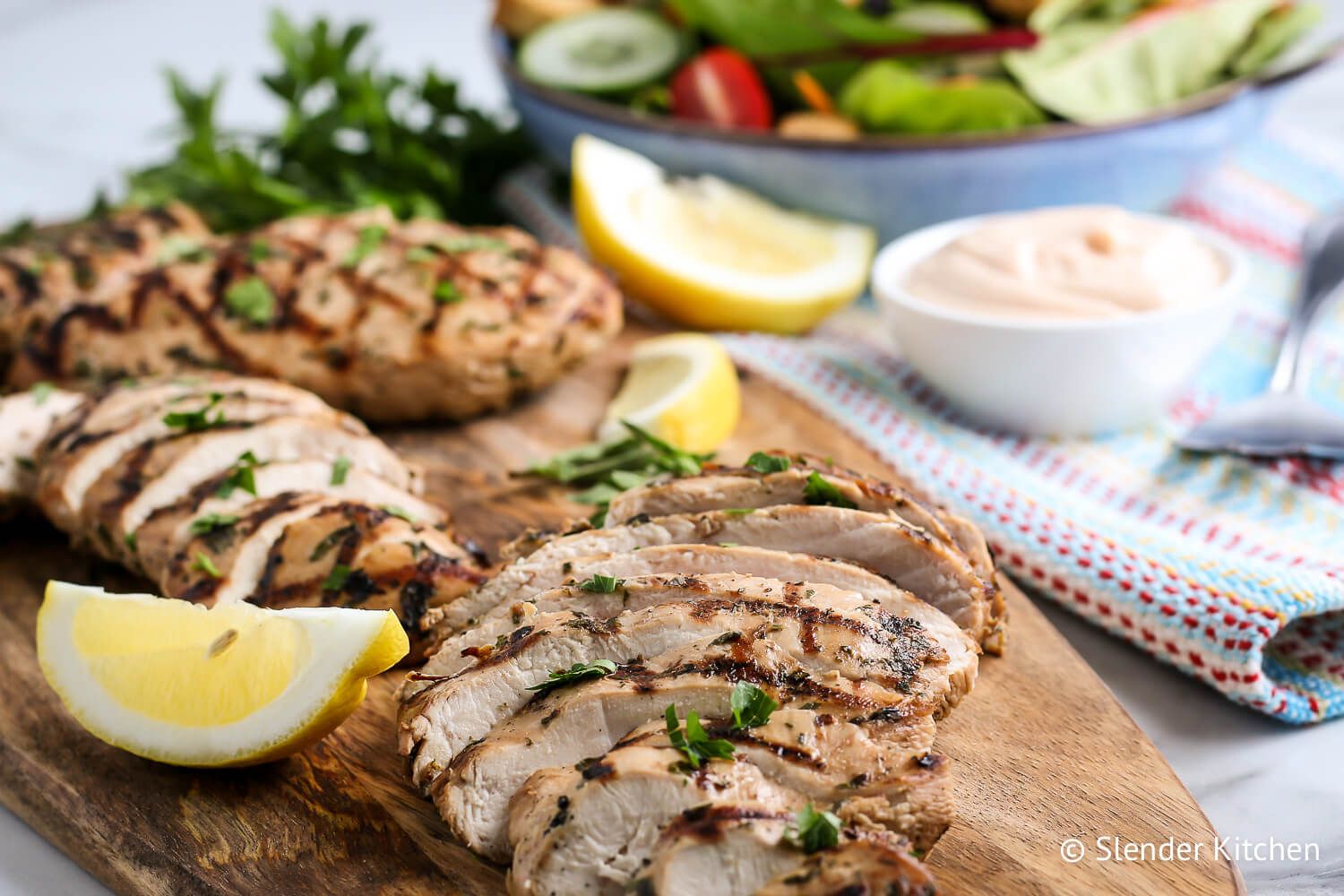 Grilled chicken breasts on a wooden cutting board with salad on the side.