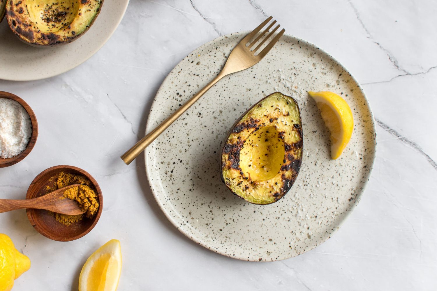 Grilled avocados on a plate with olive oil, lemon, salt, and pepper.