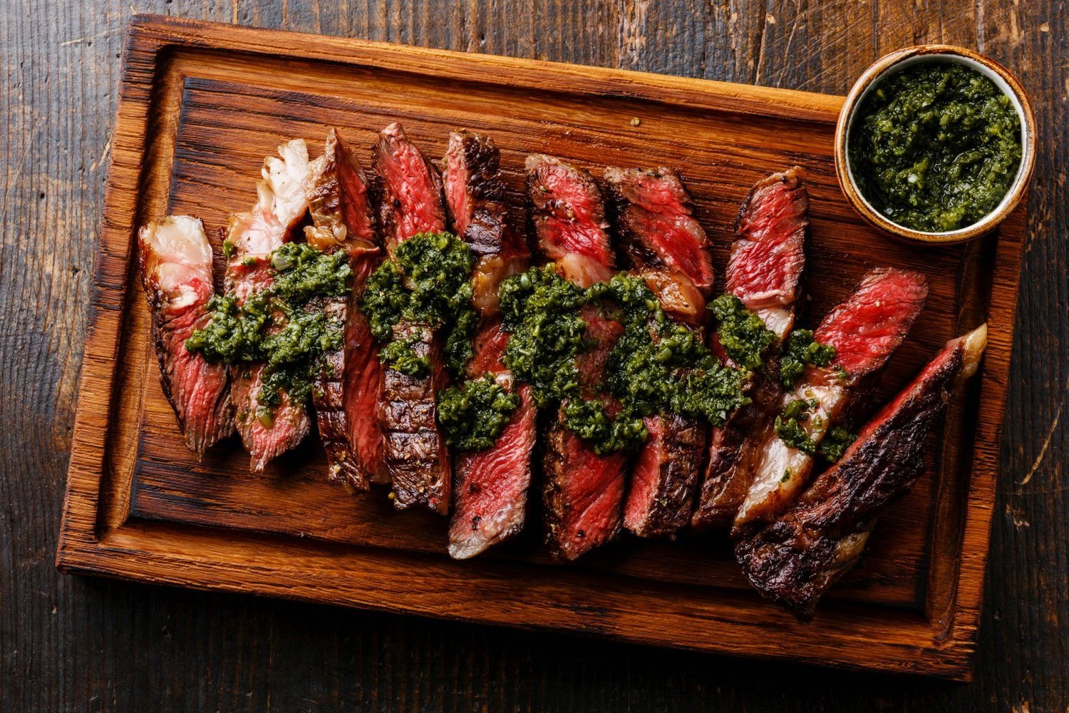 Grilled sirloin steak on a cutting board with chimichurri.