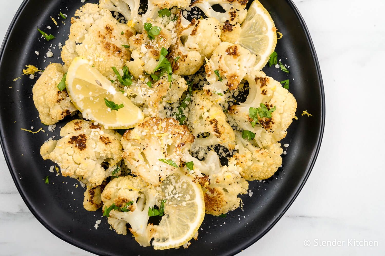 Lemon garlic roasted cauliflower with Parmesan cheese and lemon slices on a black plate.