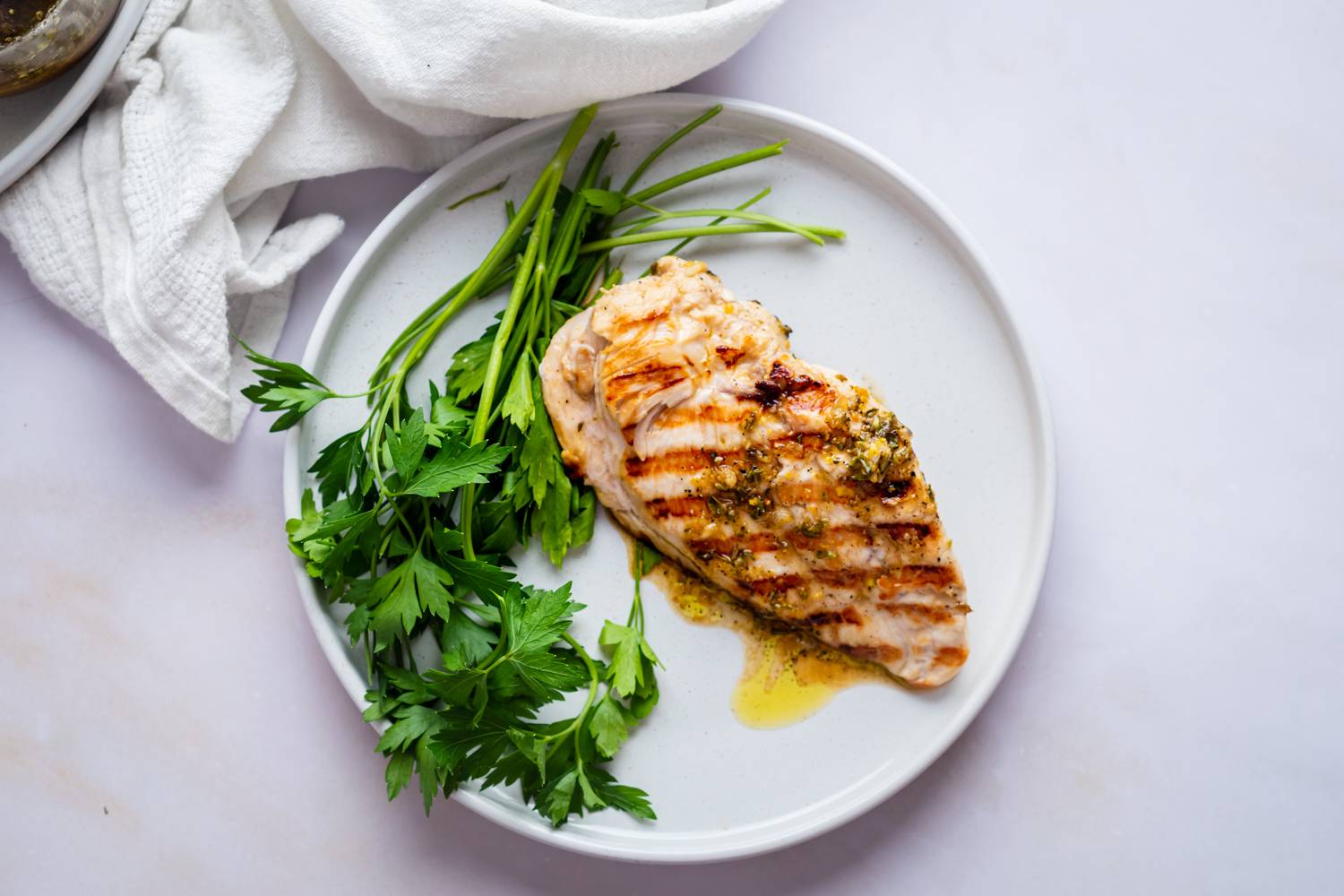 Grilled chicken breast with herb seasoning, served on a white plate with fresh parsley. Simple and appetizing presentation on a light background.