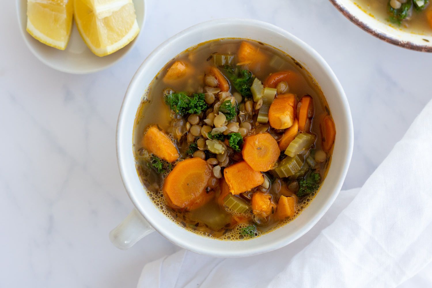 Lentil soup with cooked green lentils, carrots, onions, and celery served in a bowl with herbs,