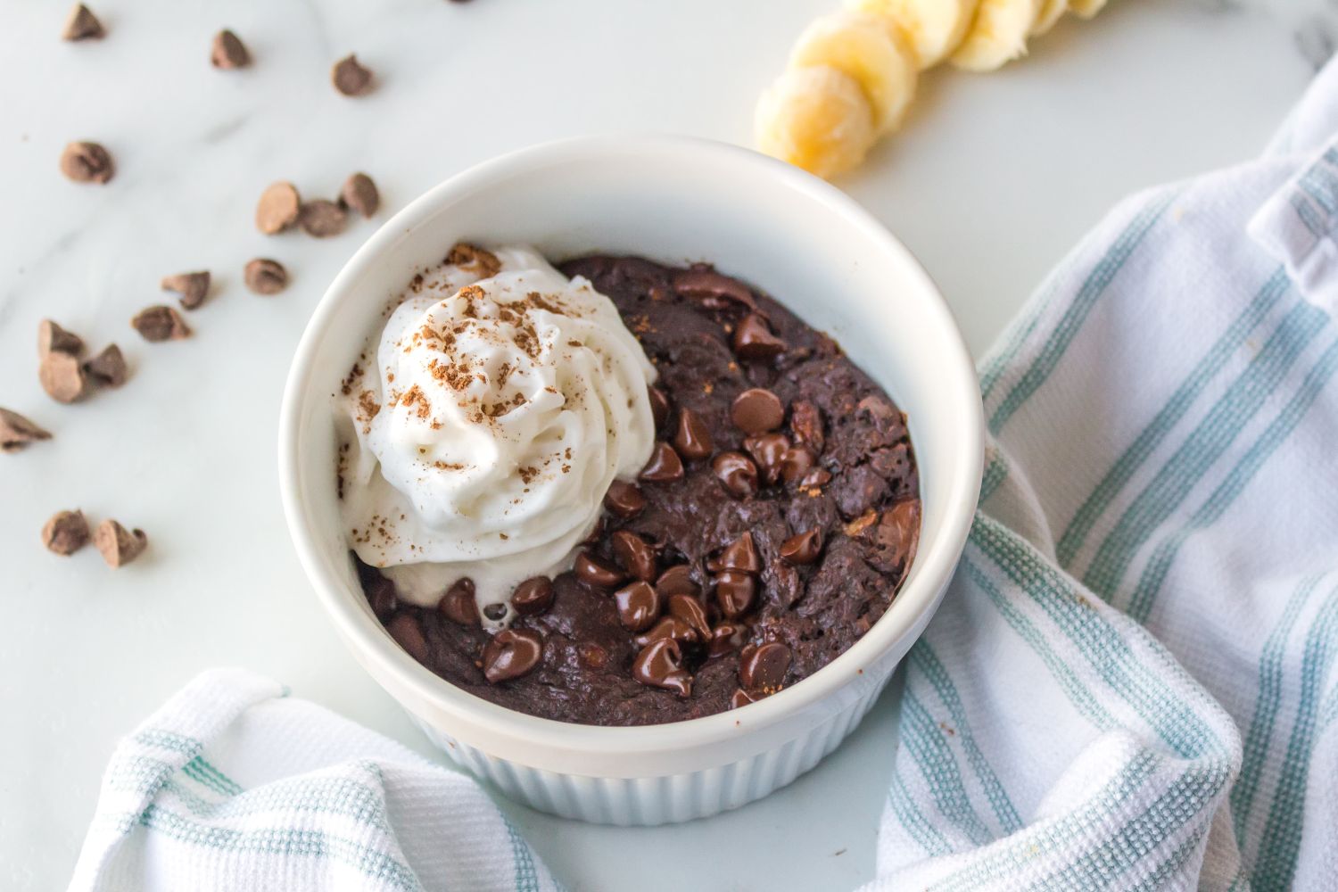Microwave chocolate peanut butter cake with banana, chocolate chips, and whipped cream in a ramekin.