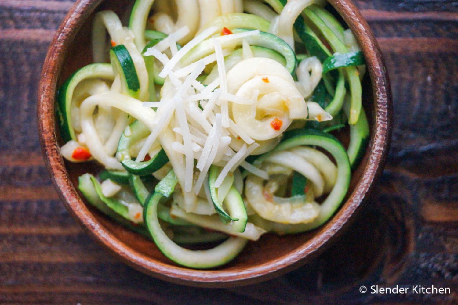 Parmesan zucchini noodles with shredded Parmesan cheese, red pepper flakes, and black pepper in a wooden bowl.