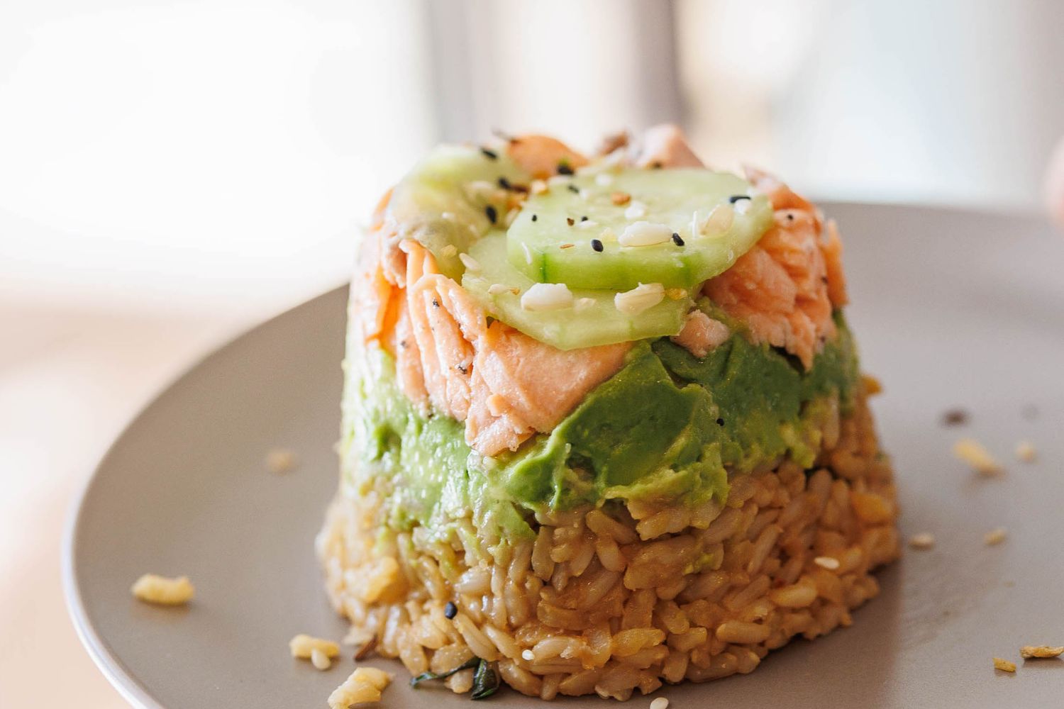 Salmon sushi stack with brown rice, avocado, salmon, and cucumbers topped with sesame seeds.