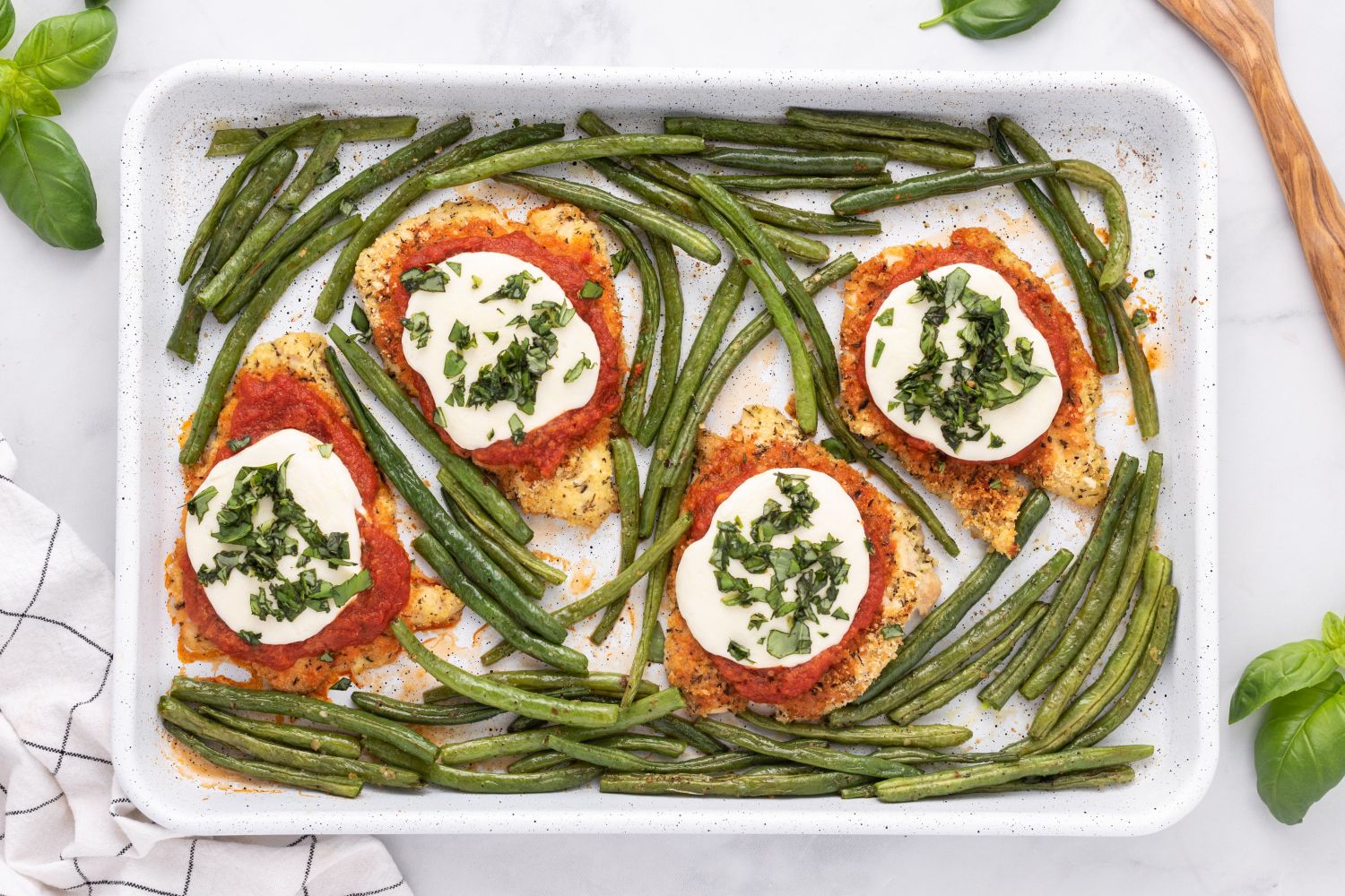 Healthy Chicken Parmesan with breaded chicken covered in sauce and cheese on a sheet pan with roasted green beans.