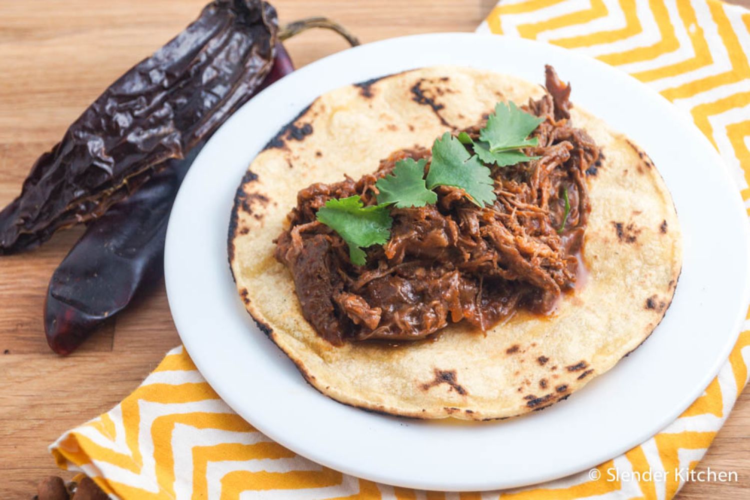 Slow cooker beef adobado with shredded beef in a red chile sauce served in a corn tortilla.