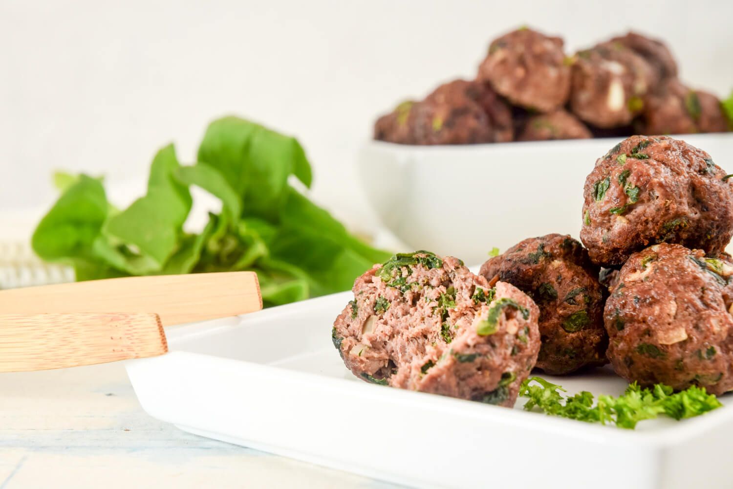 Spinach meatballs with lean beef and chopped spinach on a plate with tongs.