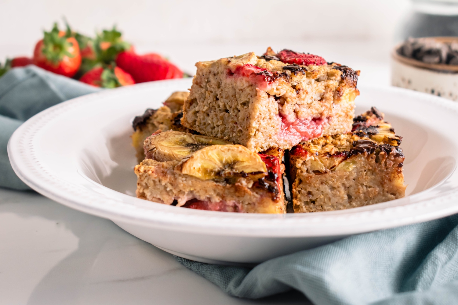 Strawberry baked oatmeal with banana and chocolate chips cut into squares and placed on a white plate.