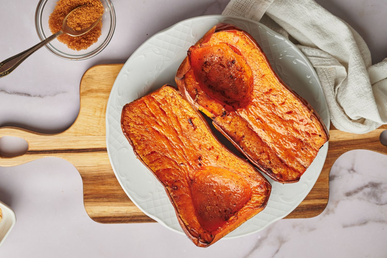 Whole roasted butternut squash hlaves served on a plate with olive oil, salt, pepper, and brown sugar.