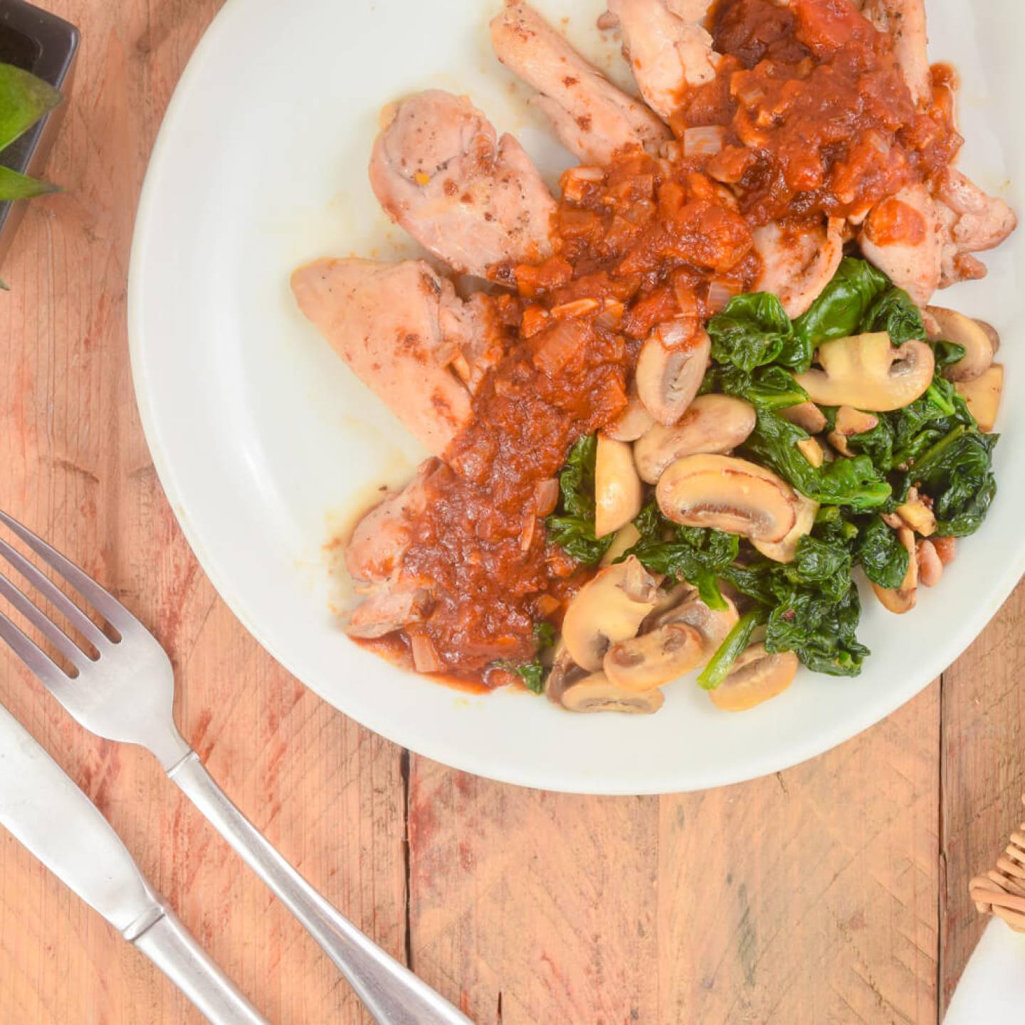 Balsamic chicken thighs with spinach and mushrooms on a plate with a napkin, fork, and knife.