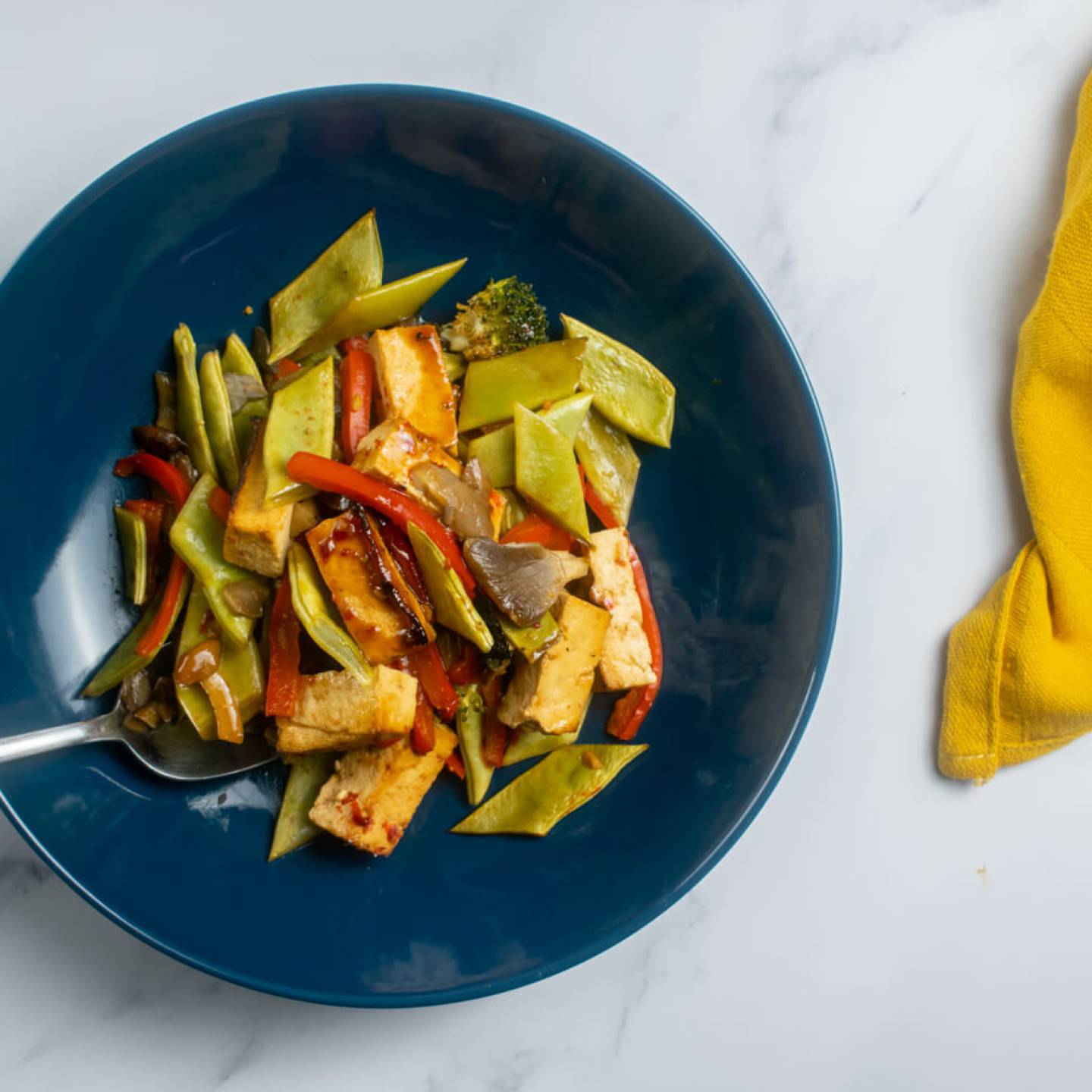 Sheet pan asian tofu with vegetables in a blue bowl with a yellow napkin.