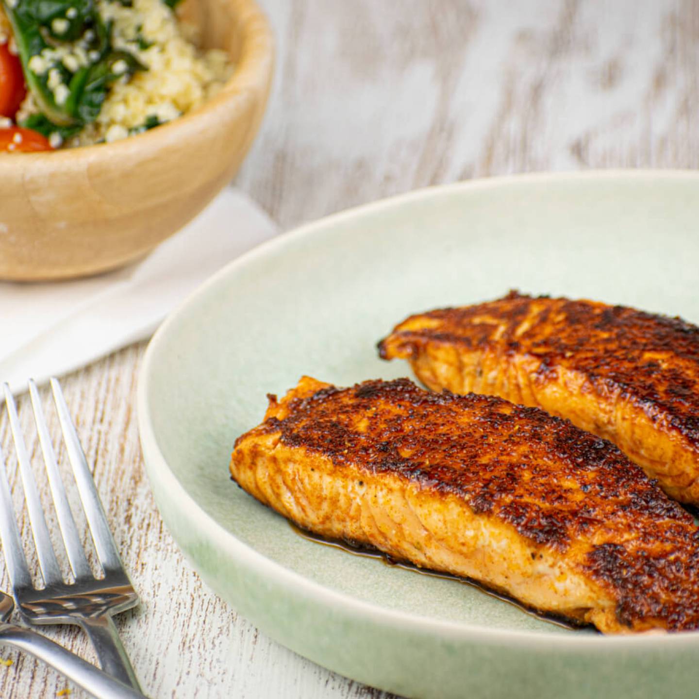 Sweet and spicy salmon with a spice crust on a plate with salad in the background.