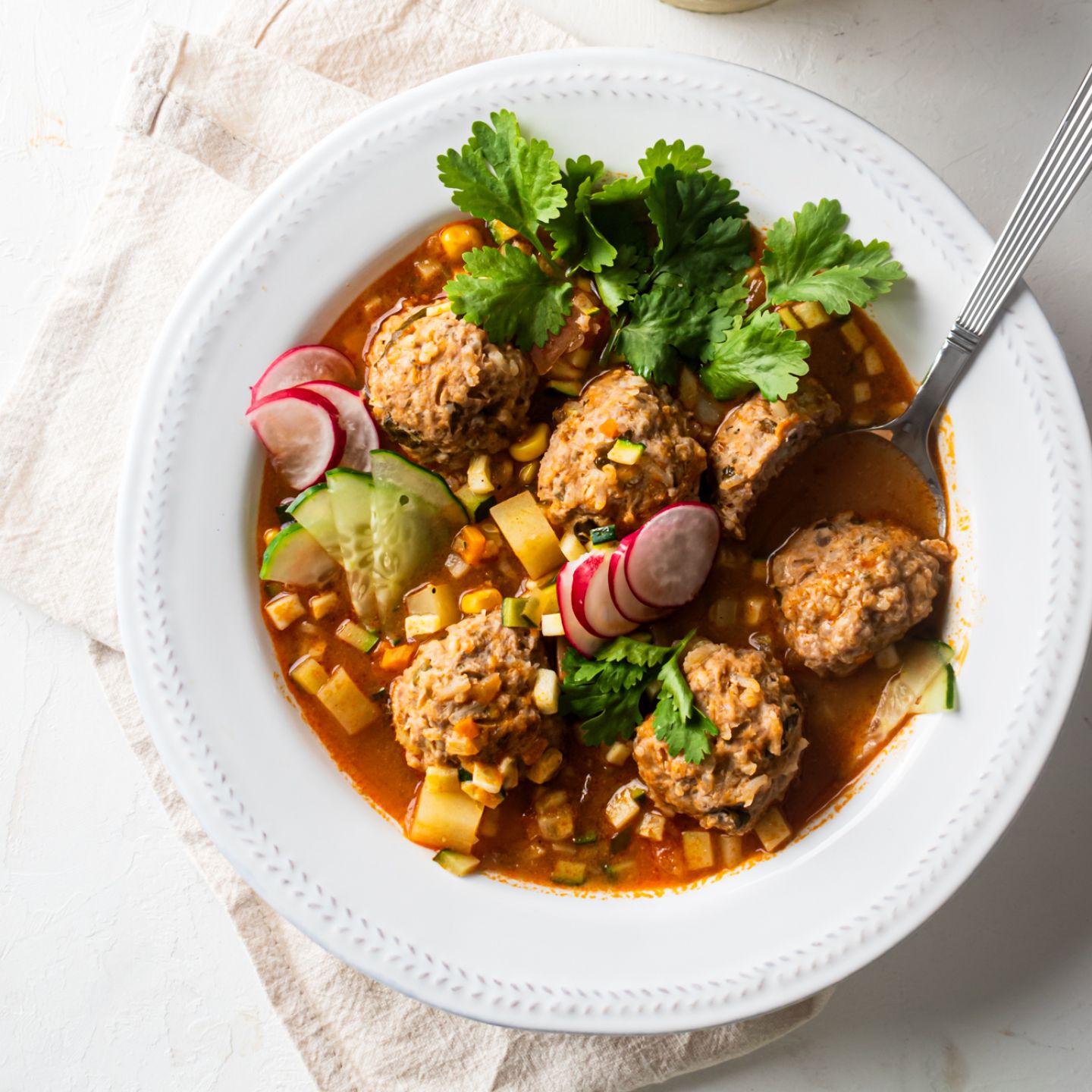 Albondigas soup with Mexican beef meatballs, carrots, zucchini, corn, and onions in tomato broth in a white bowl with cilantro.