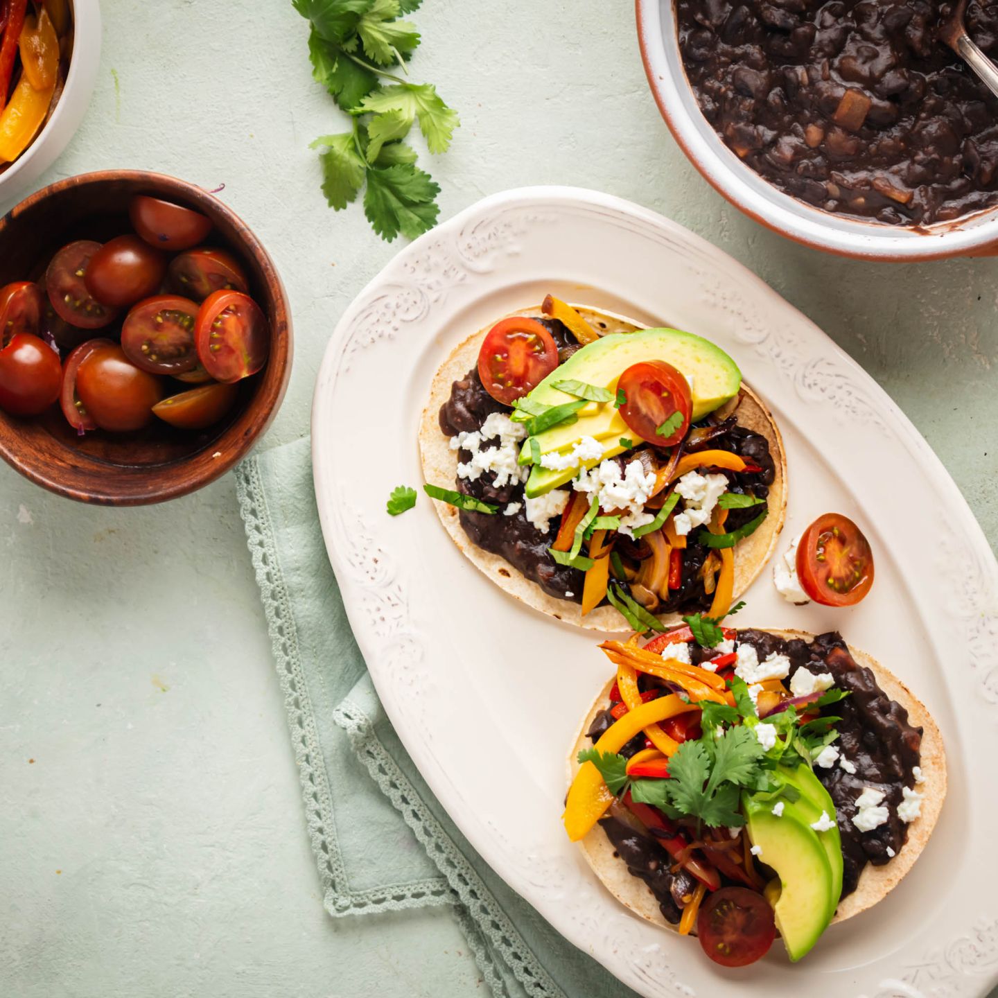 Black bean tostadas served on crispy baked tostada shells with peppers, onions, avocado, cheese, and tomatoes.