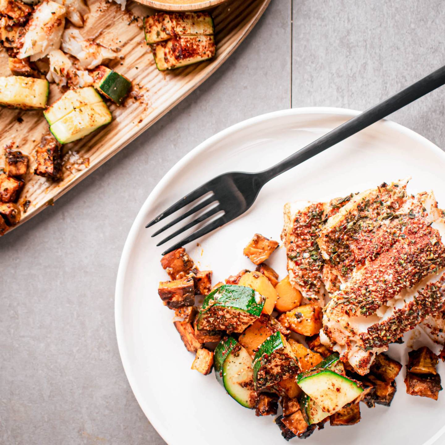 Blackened cod with vegetables cooked on a sheet pan and served on a plate with a fork.