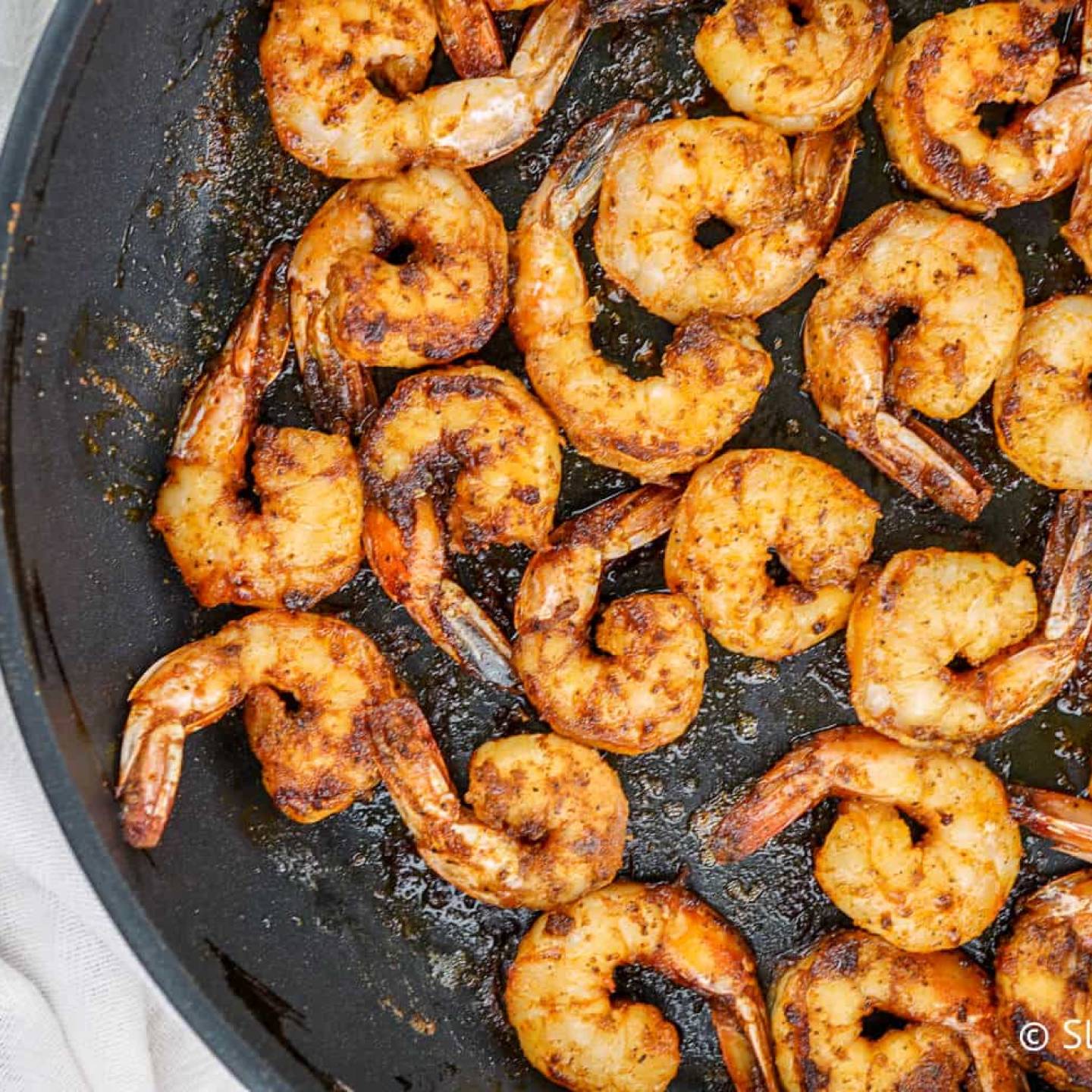 Blackened shrimp with homemade seasoning in a black skillet with butter.