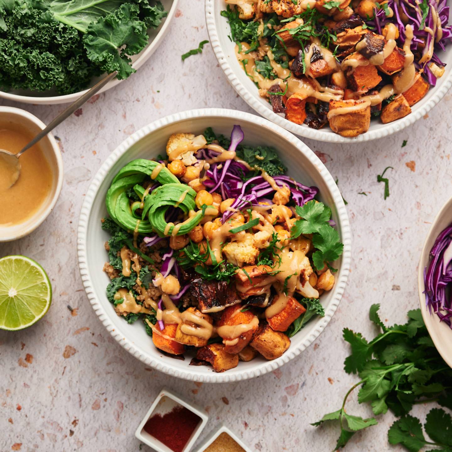 Buddha bowl with kale, chickpea, sweet potatoes, onions, and avocado served with maple tahini dressing.