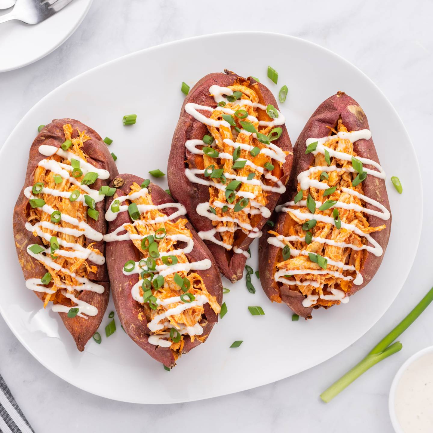 Buffalo chicken stuffed sweet potatoes on a plate with ranch dressing and green onions.
