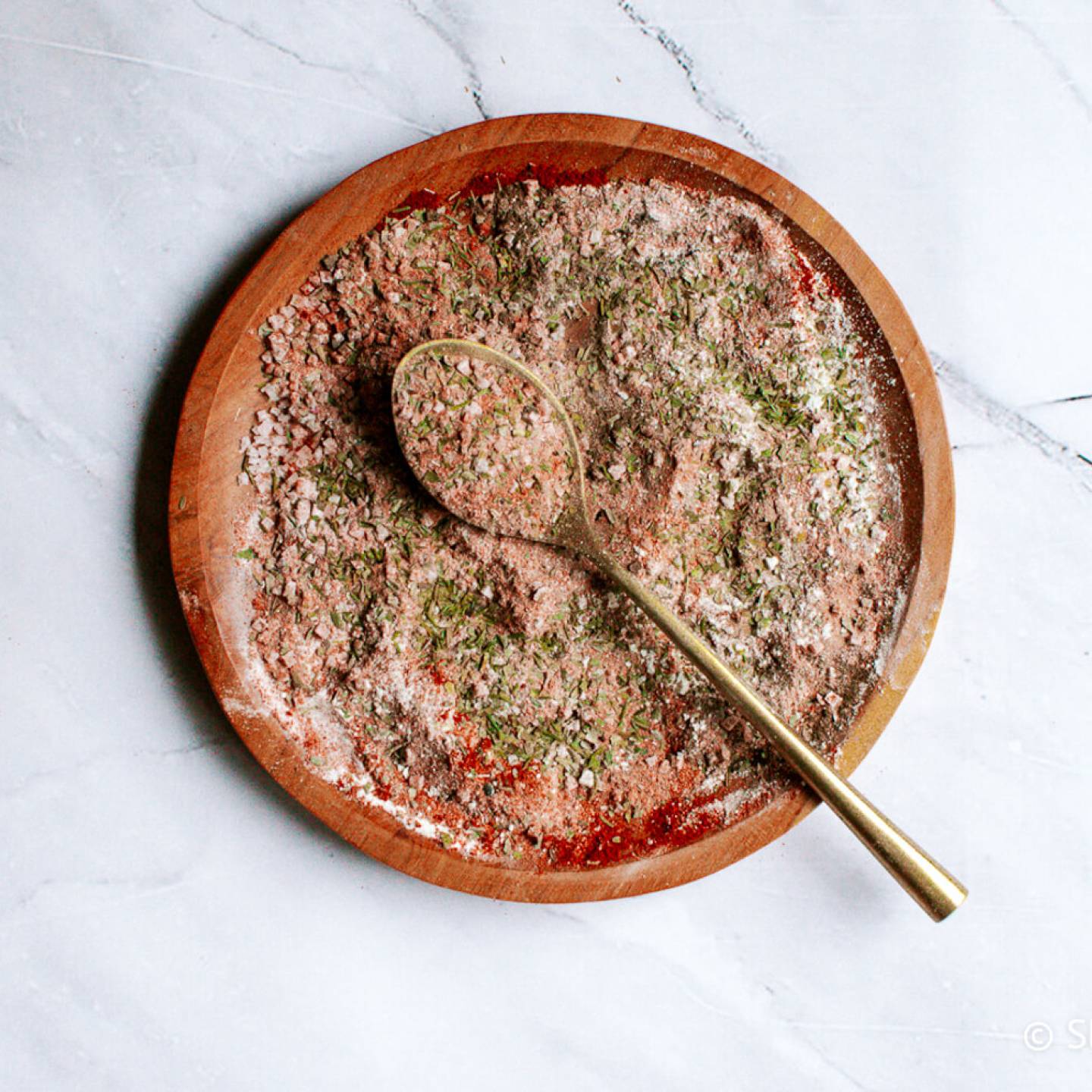 Cajun seasoning blend with smoked paprika, garlic powder, onion powder, oregano, and thyme on a wooden plate with a gold spoon.